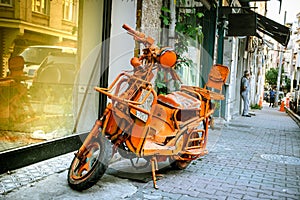 An almost scrapped modified scooter, retro city bike, painted all orange, phosphorous, stays as an offbeat object on the street.