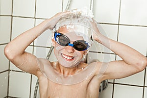 Scrawny boy in blue goggles scrubs his hair