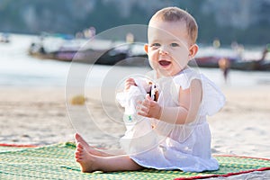 Screaming baby girl in white dress. Infant sitting on the sandy tropical beach