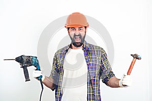 Screaming builder in helmet. Bearded man holding drill and hammer. Butal builder man. Construction worker in hard hat