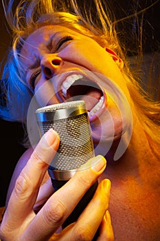 Screaming female vocalist under gelled lighting sings with passion into condenser microphone