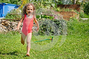 Screaming girl in red swimsuit running through sprinkler water