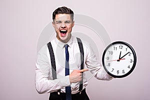 Screaming man in business clothes holding and pointing at clock over white background