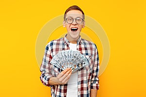 Screaming man in a plaid shirt holds money in his hands and looks into the camera on a yellow background