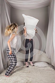 Screaming mother and daughter having fun and fighting with pillows at home