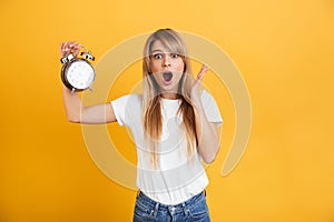 Screaming shocked young blonde woman posing isolated over yellow wall background dressed in white casual t-shirt holding alarm
