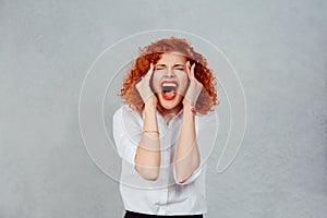 Screaming stressed. Portrait frustrated shocked redhead business woman yelling eyes closed hands on head temper tantrum isolated