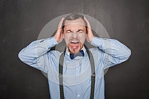 Screaming teacher man covering his ears on blackboard