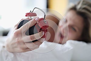 Screaming woman in bed with a red alarm clock in her hand