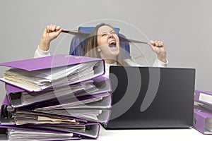 Screaming woman at desk with laptop and folders. Female entrepreneur suffers from nervous breakdown caused by fatigue, too much