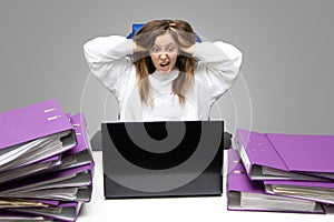 Screaming woman at desk with laptop and folders. Female entrepreneur suffers from nervous breakdown caused by fatigue, too much