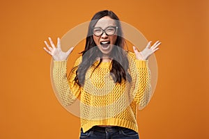 Screaming woman in glasses with hands up on empty orange background