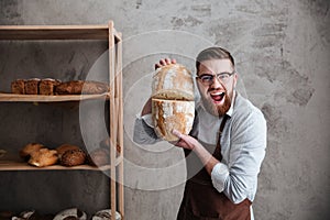 Screaming young man baker standing at bakery holding bread