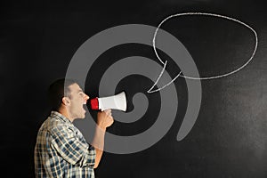 Screaming young man with megaphone near drawn speech bubble on dark background