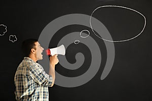 Screaming young man with megaphone near drawn speech bubble on dark background