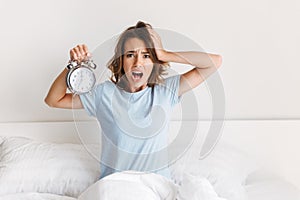 Screaming young woman holding alarm clock