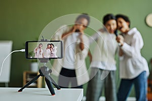 Screen of smartphone on tripod with three schoolkids performing song together