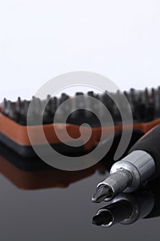 Screwdriver with phillips head with various bits in a case in the background reflected