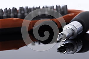 Screwdriver with phillips head with various bits in a case in the background reflected