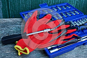 A screwdriver with red work gloves lies on a blue box with a set of tools