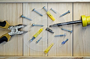 Screws, dowels, screwdriver and pliers lie on a wooden surface