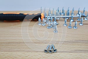 screws and screwdrivers arranged on wooden background close-up view