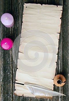 Scroll paper with place for text pen for writing and inkwell on a rough wooden table in the light of burning candles