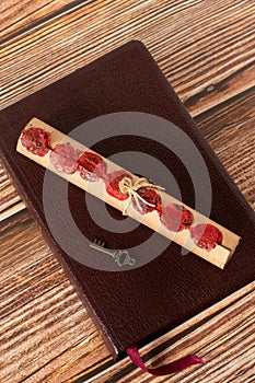 Scroll with seven seals and old key on top of closed holy bible book placed on wooden table, vertical shot