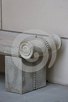 Scrolled and beaded end of gray concrete bench against block wall photo