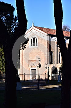 Scrovegni Chapel, illuminated by the sun, with pine trees in the shade and with the background of the blue sky in Padua.