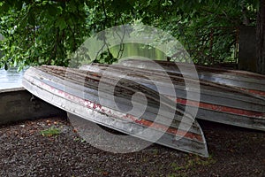 scruffy row boats lying upside down on the shore of a lake