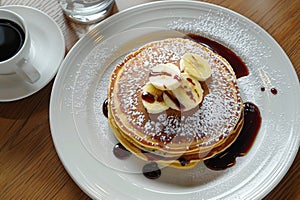 Scrumptious chocolate pancakes with a ripe banana elegantly arranged on a white plate, top view photo