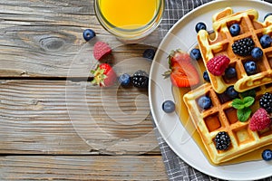 Scrumptious waffles with syrup, berries and orange juice on wooden table for breakfast, top view photo