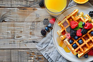 Scrumptious waffles with syrup, summer berries and orange juice on rustic wooden table, top view photo