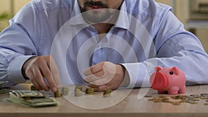 Scrupulous bachelor planning his monthly budget, putting coin in piggy bank