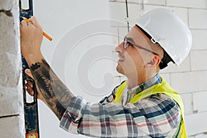 Scrupulous construction engineer in a white helmet making marks on the wall