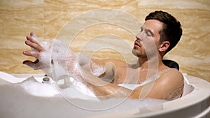 Scrupulous man soaping himself with loofah, taking bath with foam, cleanness photo