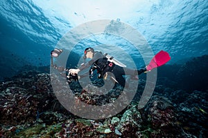 Scuba diver with camera diving over coral reef in Thailand