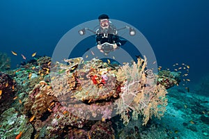 Scuba diver with camera diving over coral reef in Thailand