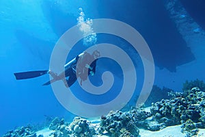 Scuba diver descending in to the sea, three boats silhouettes above him