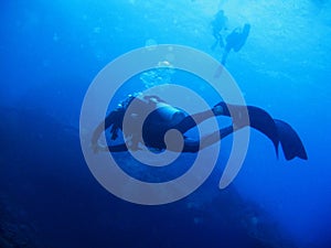 Scuba diver with full equipment is underwater. Sunlight and bubbles. Two scuba divers are on the background