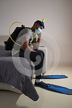 Scuba diver in medical mask sitting on bed