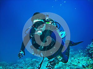 Scuba diver is underwater. He is wearing in full scuba-diving equipment: mask, regulator, BCD, fins. Diver is on the blue water ba