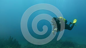 Scuba diver woman in motion, with a flashlight in her hand surrounded by a clean blue seabed near the bottom. Space for text, ads