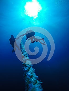 Scuba Divers Descending Holding a Rope to a Shipwreck in the Red Sea in Egypt.