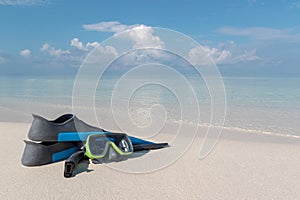 Scuba goggles and flippers on a white beach. Clear blue water as background