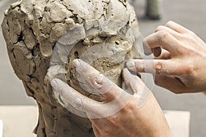 sculptor creates a bust and puts his hands clay on the skeleton of the sculpture