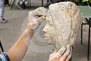Sculptor creates a bust and puts his hands clay on the skeleton of the sculpture.