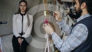 Sculptor creating sculpture of human`s face on canvas while young woman posing him in art studio