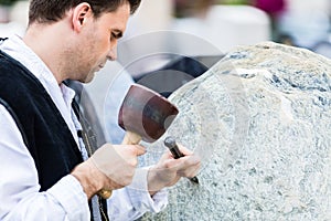 Sculptor with mallet and cutter working on erratic block